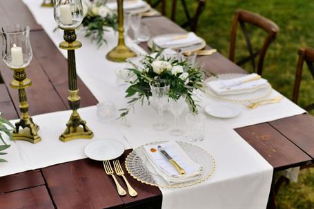Top view of glassware and cutlery on the wooden table outdoors, with white eustomas and ruscus bouquets